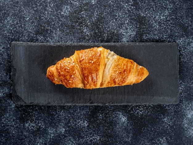 Croissant fourré à la crème allongé sur une planche à découper en ardoise sur un fond sombre