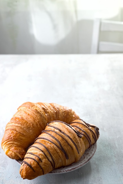 Croissant fraîchement sorti du four, décoré avec une sauce au chocolat isolée sur un fond gris ardoise