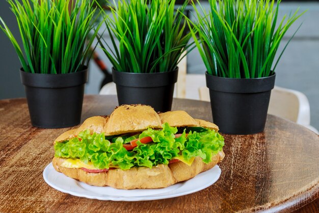 Croissant frais au jambon et feuille de salade avec salade fraîche sur table en bois.