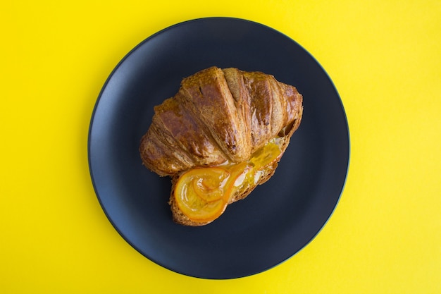 Croissant avec marmelade d'orange dans la plaque noire sur fond jaune. Vue de dessus.