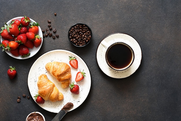Croissant à la pâte de chocolat et une tasse de café, fraises sur la table de la cuisine. • Collation traditionnelle ou petit déjeuner.