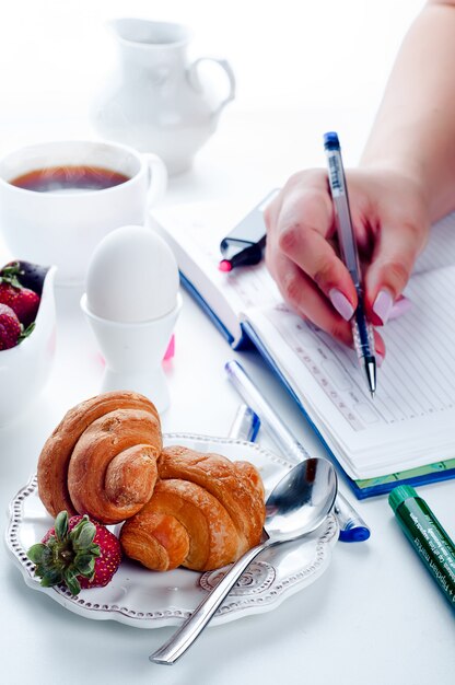 croissant de petit déjeuner et cahier sur une table blanche