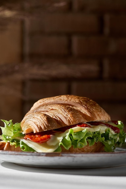 Croissant de petit-déjeuner délicieux et sain avec poulet, tomates, laitue et fromage à la crème sur une assiette