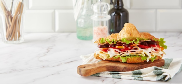 Croissant sandwich au fromage jambon laitue tomates olives et délicieuse sauce sur planche de bois