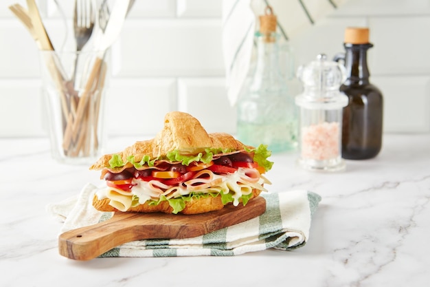 Croissant sandwich au fromage jambon laitue tomates olives et délicieuse sauce sur planche de bois