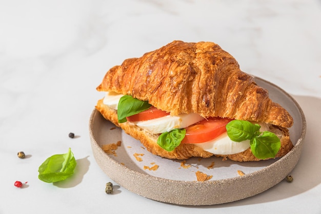 Croissant sandwich à la tomate mozzarella et basilic dans une assiette sur fond blanc Petit-déjeuner italien