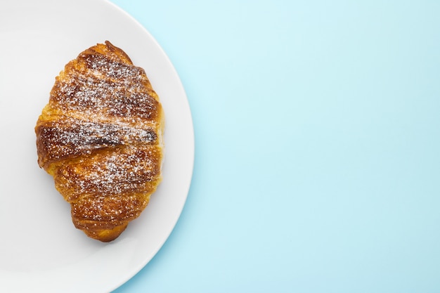 Croissant savoureux avec du sucre en poudre sur la croûte brune sur fond bleu