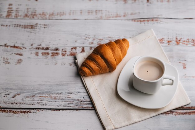 Croissant et une tasse de café blanche sur une table en bois