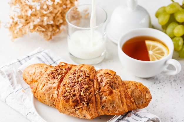 Croissant et thé pour le petit déjeuner sur fond blanc.