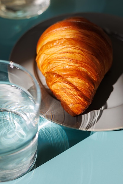 Photo croissant et un verre d'eau et sur une table bleue pour le petit-déjeuner à la maison ou au café-restaurant