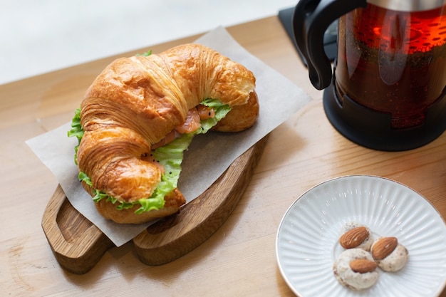 Des croissants au saumon et salade fraîche sont servis sur une planche de bois pour le déjeuner. Thé noir dans une théière. Nourriture de remise en forme dans un café.