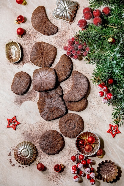 Croissants de chocolat de biscuits sablés de Noël traditionnels faits maison avec du sucre glace au cacao avec des moules à biscuits, sapin, décorations d'étoiles de Noël rouges. Surface en marbre rose. Mise à plat