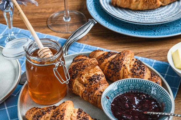 Croissants avec confiture et miel sur une table en bois.