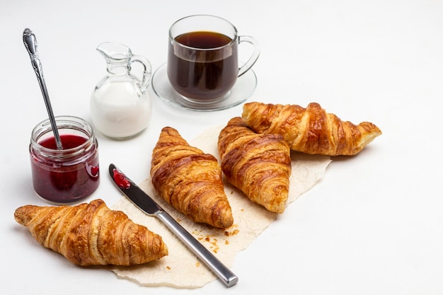 Croissants et couteau sur papier. Tasse de café. Crème en crème. Confiture en bocal. Vue de dessus. Fond blanc.