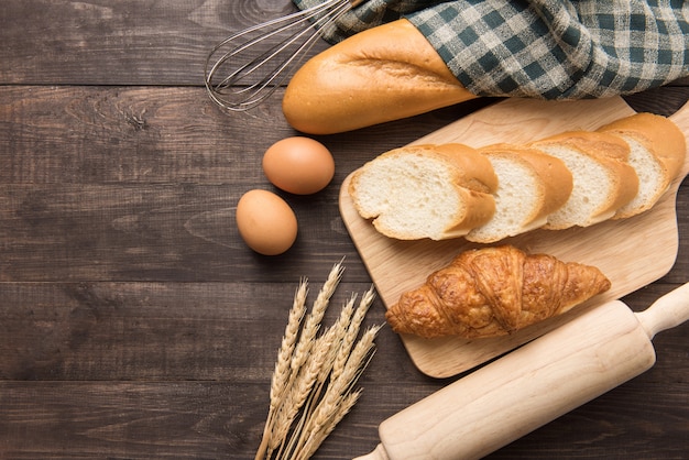 Croissants fraîchement sortis du four, baguette et œufs sur fond de bois