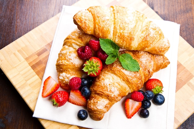 Croissants frais savoureux avec des baies sur fond de bois