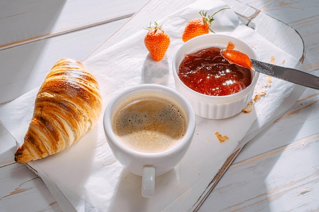 Croissants frais seulement cuits au four avec de la confiture et du café sur la table au soleil du matin délicieux petit déjeuner concept