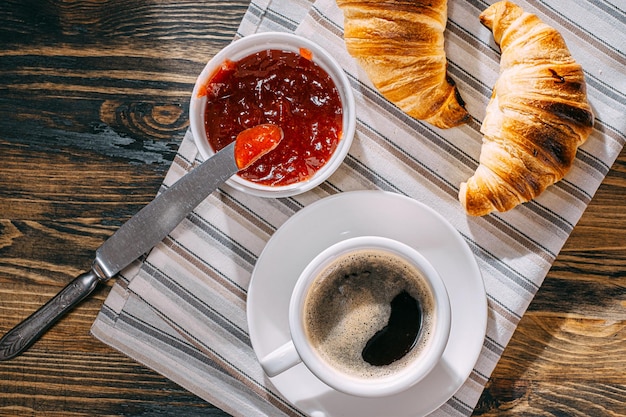 Croissants frais seulement cuits au four avec de la confiture et du café sur la table au soleil du matin délicieux petit déjeuner concept