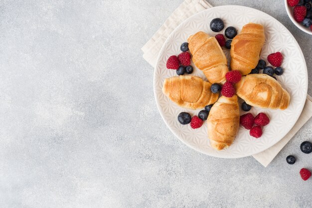 Croissants avec des framboises et des bleuets frais sur une surface de béton sombre