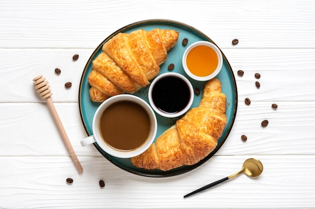 Croissants français frais sur plaque confiture de bleuets miel tasse de café sur fond de bois