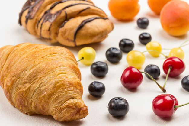 Croissants et myrtilles, cerises rouges et jaunes sur table. Surface blanche. Vue de dessus