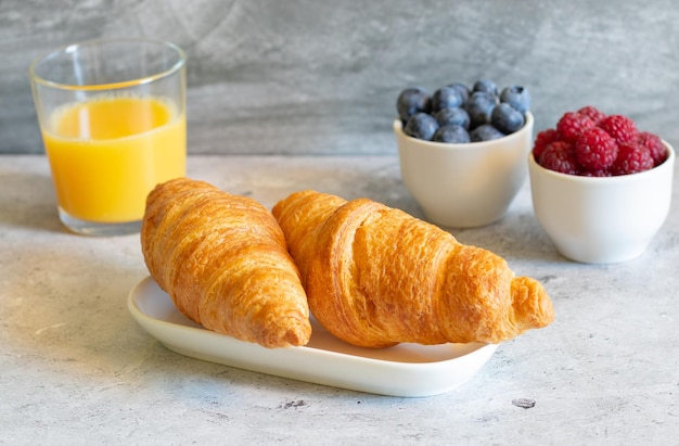 Croissants myrtilles framboises jus d'orange sur fond de béton clair