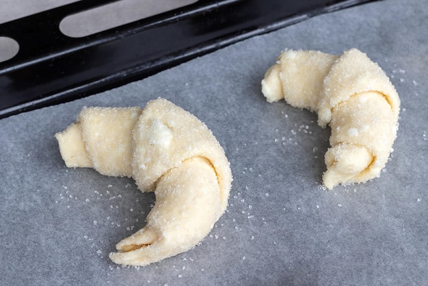 Croissants à partir d'une pâte de fromage cottage crue préparée pour la cuisson saupoudrée de sucre sur une plaque à pâtisserie recouverte de papier sulfurisé avant de les charger dans le four Processus de fabrication de bagels au caillé