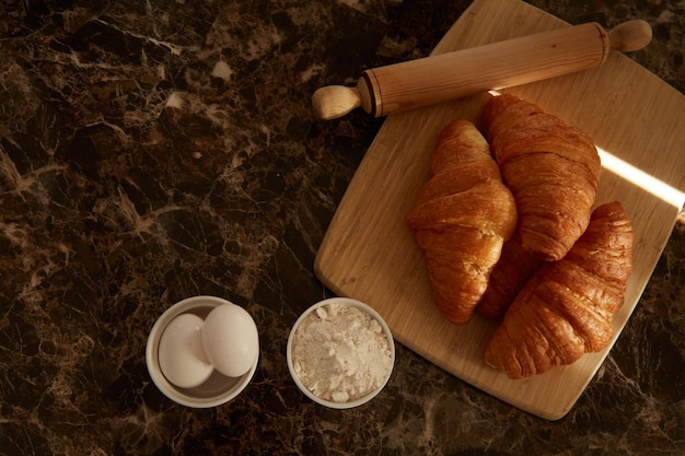 Croissants sur une planche à découper avec un rouleau à pâtisserie et quelques ingrédients sur une table. concept de flatlay, espace de copie.