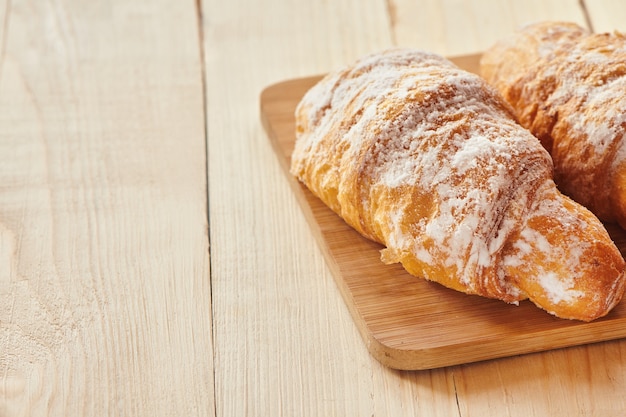 Croissants savoureux avec du sucre en poudre sur planche de bois. Pâtisserie traditionnelle française au petit déjeuner. Vue rapprochée avec espace de copie.