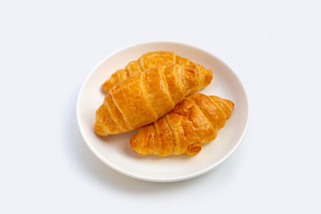 Croissants savoureux en plaque blanche sur fond blanc.