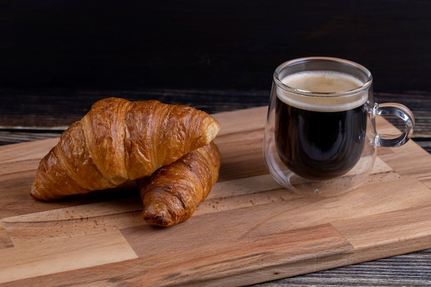 Croissants avec une tasse de café sur une planche de bois.