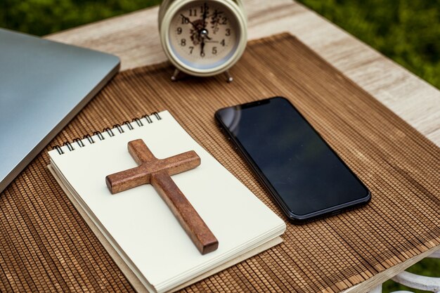 Croix en bois et carnet de notes à côté du smartphone.