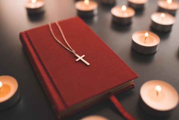 Croix chrétienne en argent sur livre de bible en papier rouge sur table au-dessus de bougies allumées en gros plan