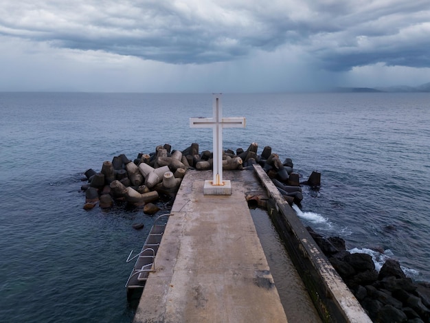 Croix chrétienne debout sur la jetée dans la mer ou l'océan avec un ciel dramatique