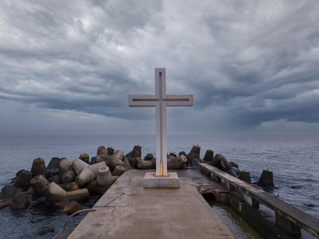 Croix chrétienne debout sur la jetée dans la mer ou l'océan avec un ciel dramatique