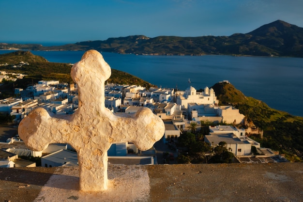 Croix chrétienne et village de plaka sur l'île de milos sur des fleurs de géranium rouge au coucher du soleil en grèce