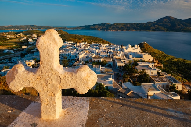 Croix chrétienne et village de plaka sur l'île de milos sur des fleurs de géranium rouge au coucher du soleil en grèce