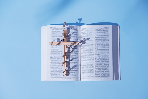 Croix décorée de fleurs avec la Sainte Bible ouverte sur fond bleu concept minimaliste de vacances de Pâques