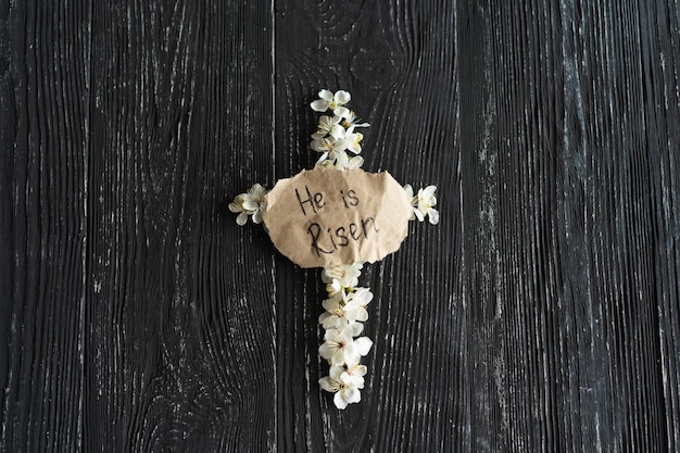 Croix avec des fleurs sur un fond en bois avec l'inscription Christ est ressuscité.