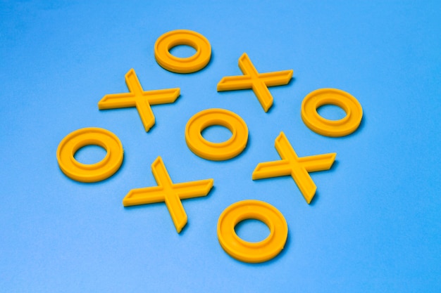 Croix et zéros en plastique jaune pour jouer au tic-tac-toe sur une surface bleue. Concept XO Win Challenge. Jeu éducatif pour les enfants