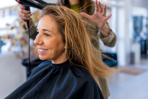 Crop coiffeur séchant les cheveux d'une femme joyeuse