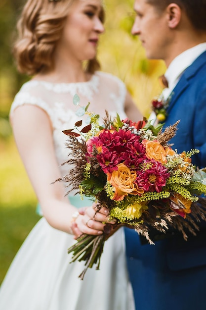 Crop floue couple juste marié dans des vêtements élégants étreignant et tenant un beau bouquet de frais