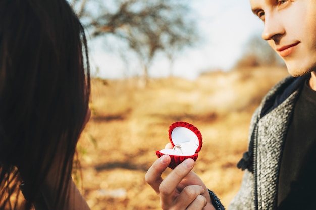 Photo crop handsome guy holding box avec élégante bague de fiançailles tout en proposant à une femme méconnaissable sur une journée ensoleillée dans la nature