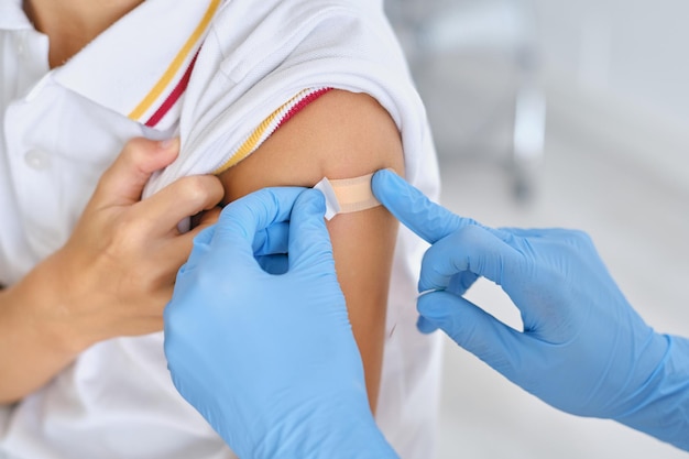 Crop infirmière méconnaissable dans des gants jetables appliquant un patch médical sur l'épaule du patient à l'hôpital