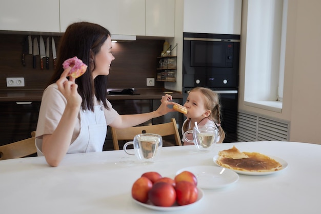 Crop shot de la mère en rouge et sa fille ayant des beignets colorés assis à la cuisine Concept de régime et malbouffe