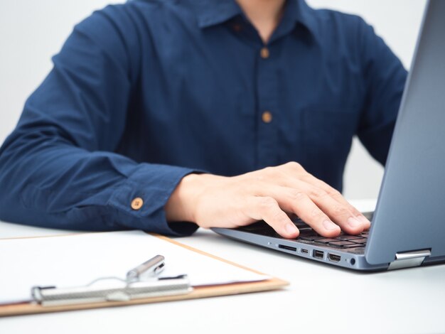 Crop shot of man using laptop on the table with document board and pen