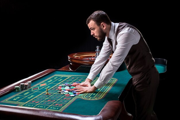 Croupier derrière une table de jeu dans un casino sur fond noir. Jeux d'argent. Casino. Roulette. Poker