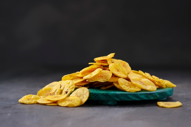 Croustilles de banane séchées ou gaufrettes de banane dispersées sur une base ronde verte avec fond texturé gris isolé