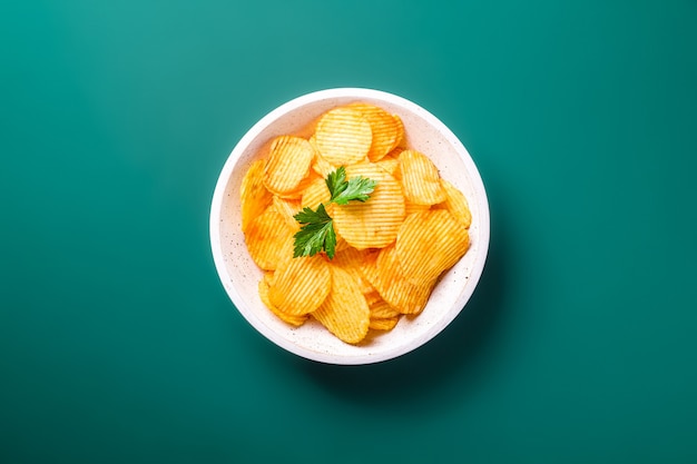 Croustilles frites dorées ondulées avec feuille de persil dans un bol en bois sur vert