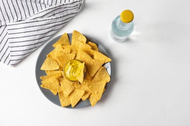 Croustilles de maïs nachos avec sauce au fromage sur la vue de dessus de table blanche, bouteille de boisson gazeuse, serviette à rayures